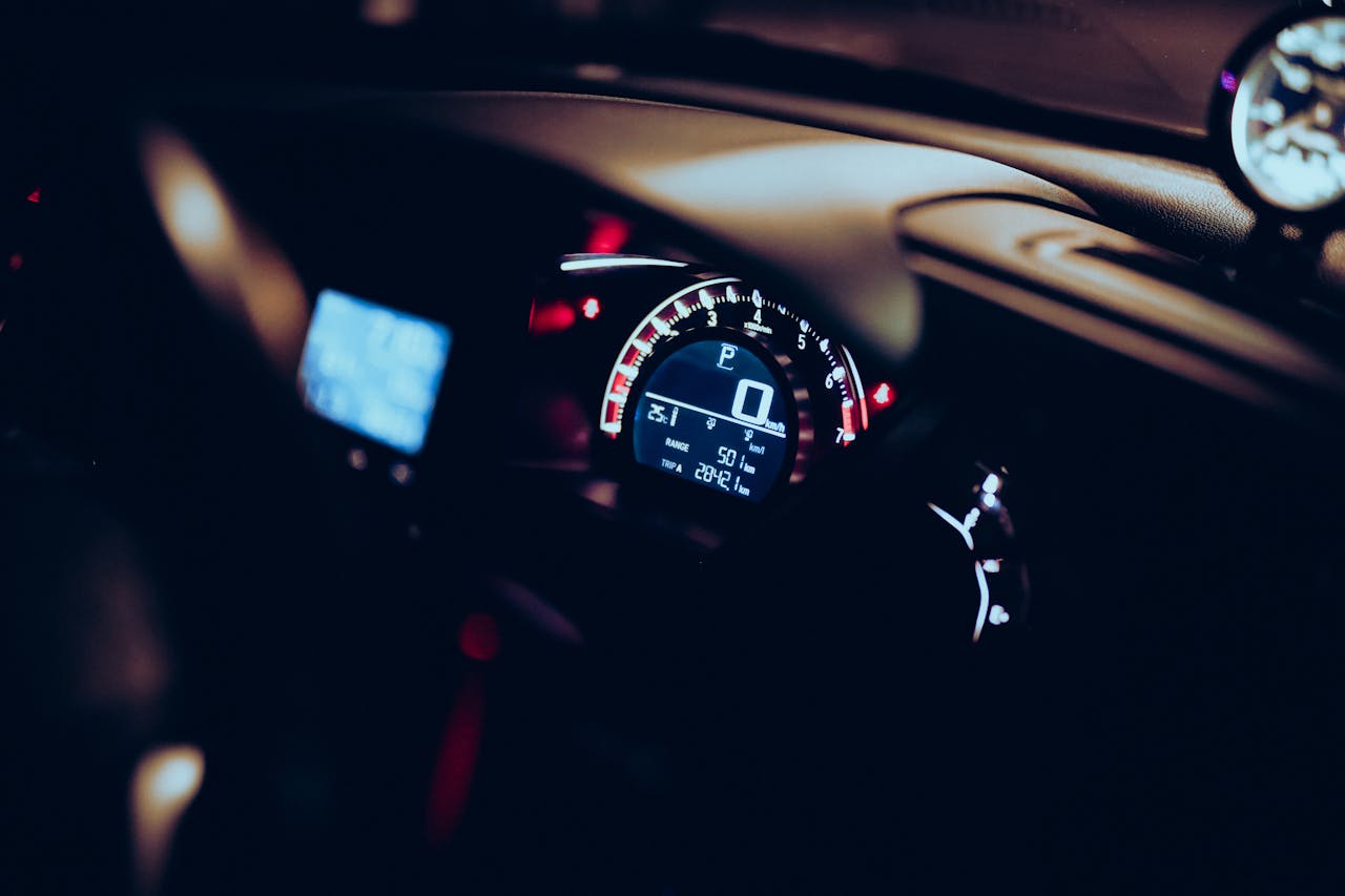 about-us-01 Close-up of a car dashboard at night with illuminated speedometer and tech displays.